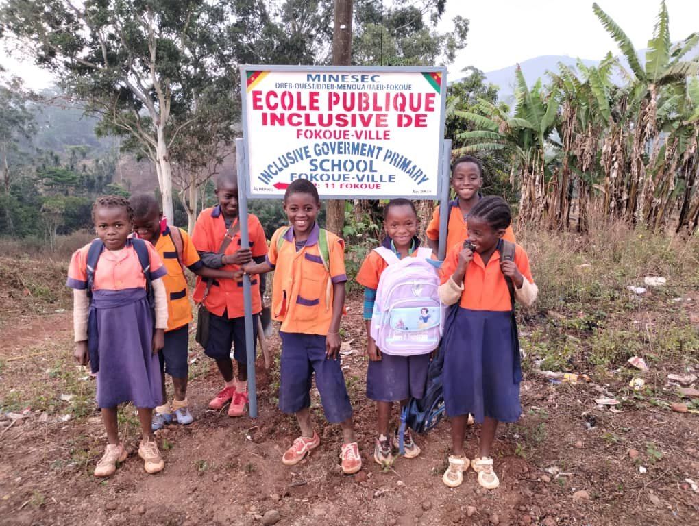 Élèves avec leurs kits devant le panneau de l'école publique inclusive de Fokoué-Ville